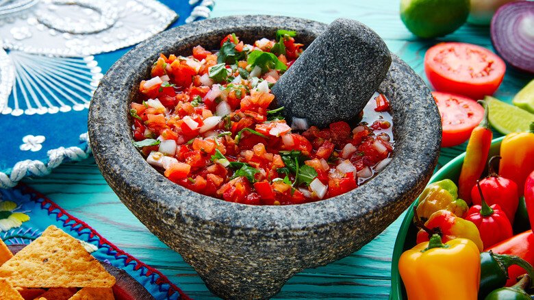 pico de gallo in a molcajete, surrounded by tomatoes and peppers