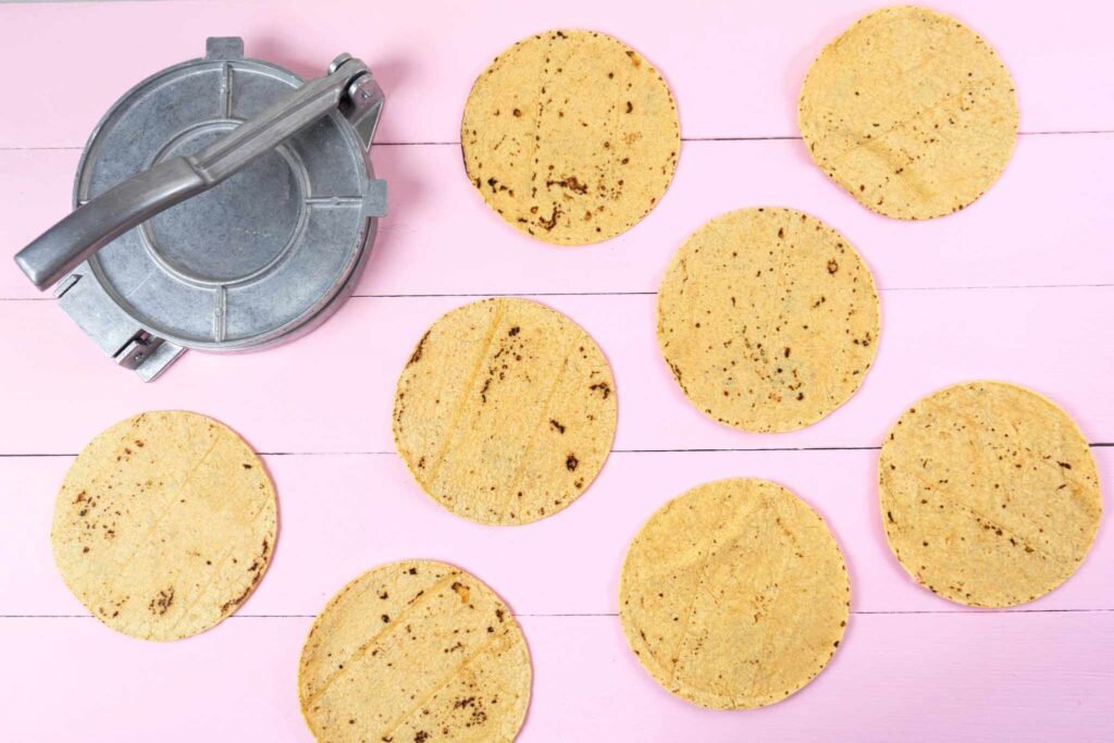 tortilla press and eight tortillas on a pink table